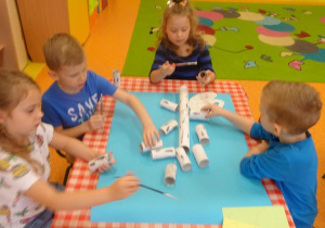 Czwórka dzieci nakleja na duży arkusz papieru rolki tworząc pień i koronę drzewa.